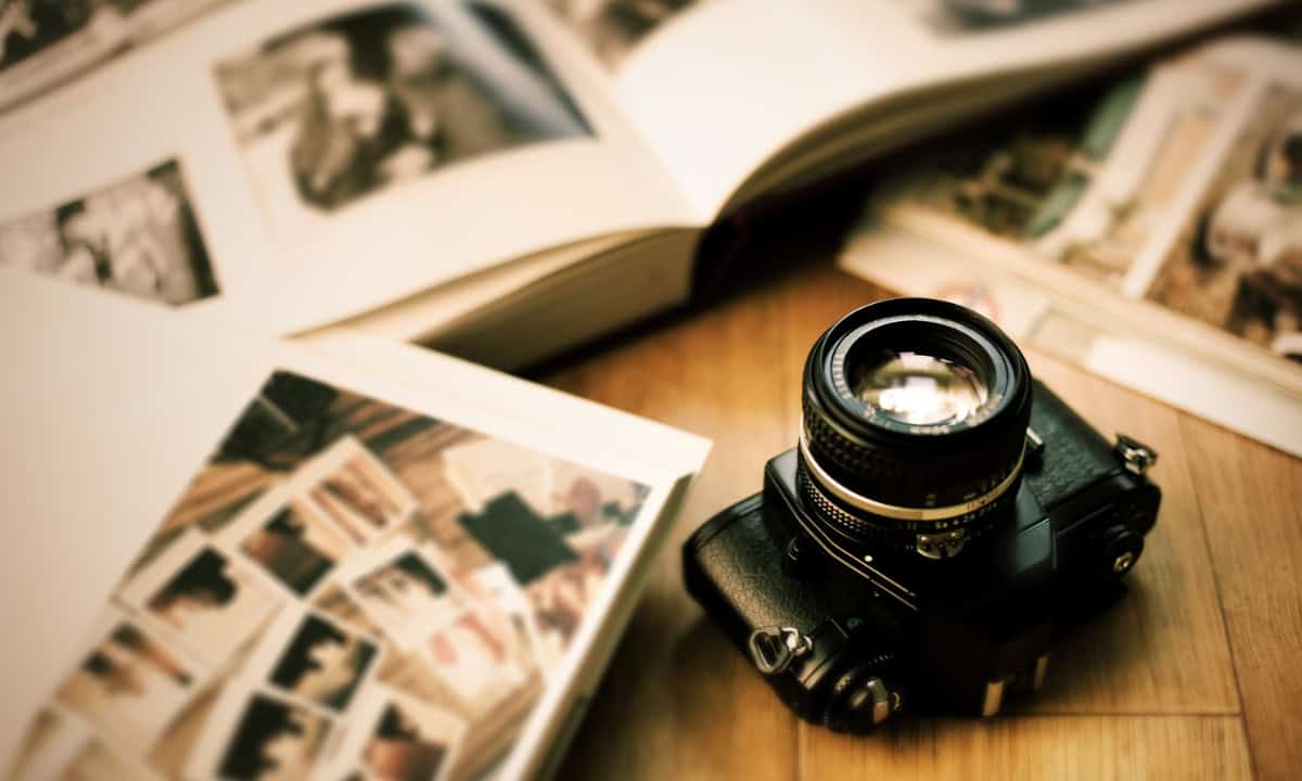 A vintage camera sits on a wooden surface next to open photo albums filled with various photographs.